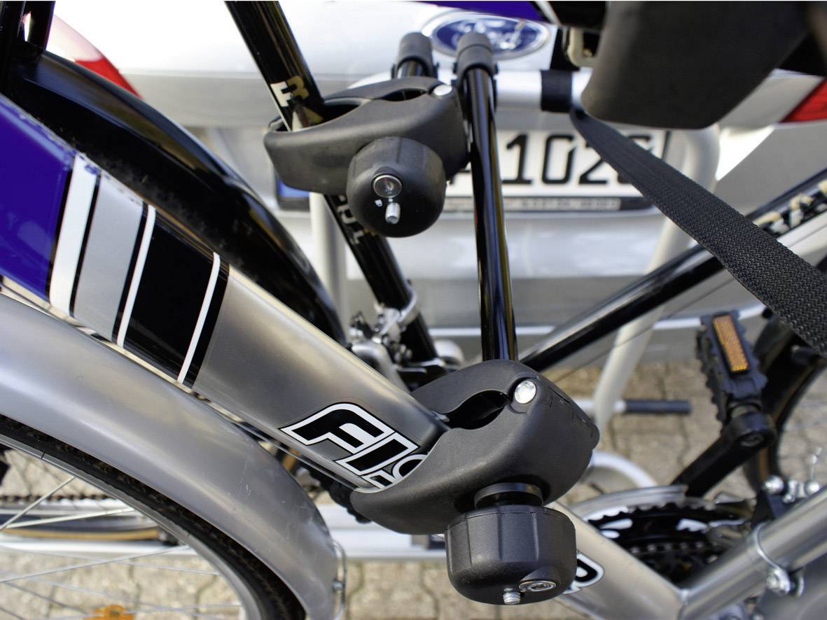 Zbliżenie roweru o srebrnej ramie, przymocowanego do czarnego bagażnika rowerowego na samochodzie. Bagażnik jest wyposażony w zamek.