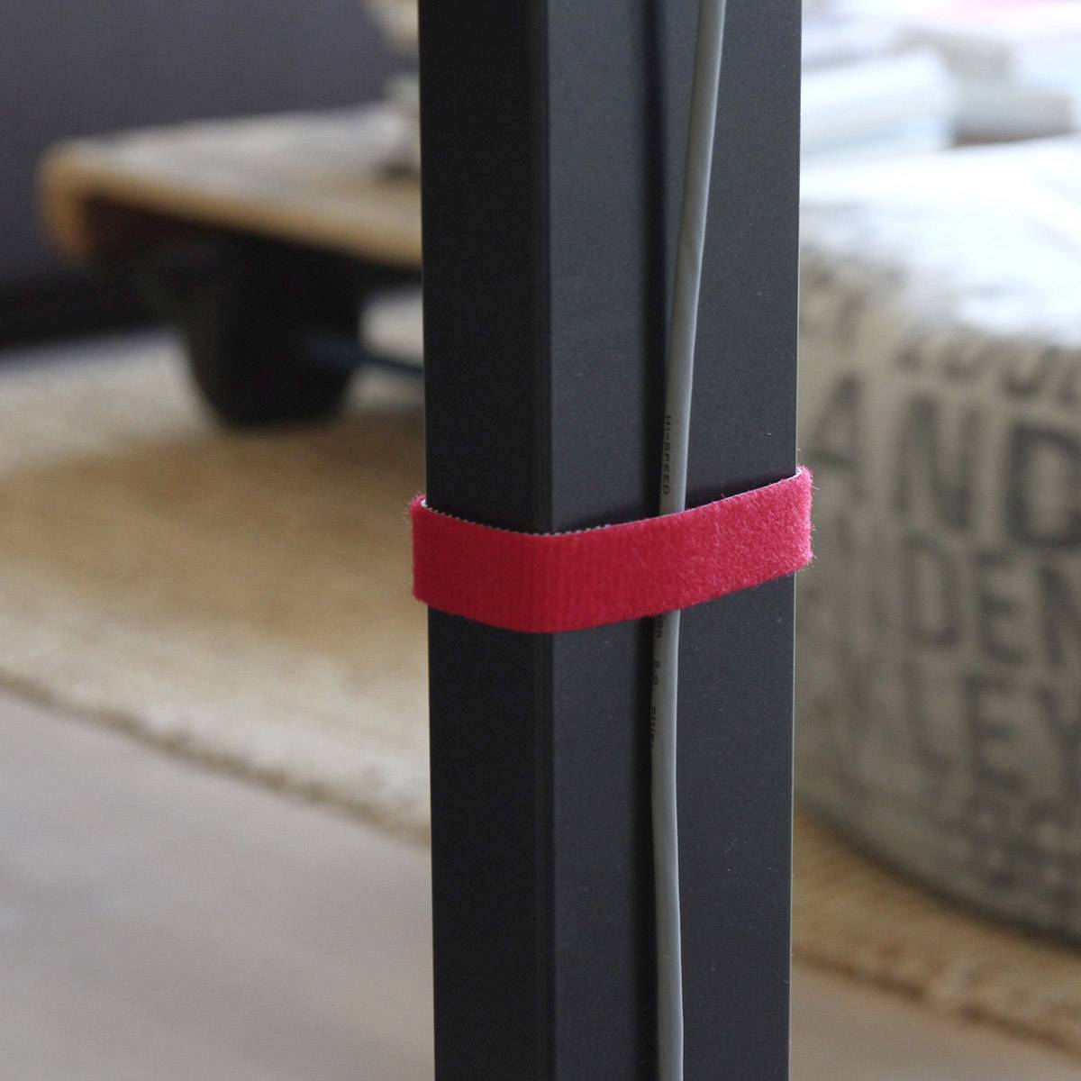 Czarna noga stołu, do której za pomocą czerwonej taśmy rzepowej przymocowane są kable. W tle nieostro widać stół.