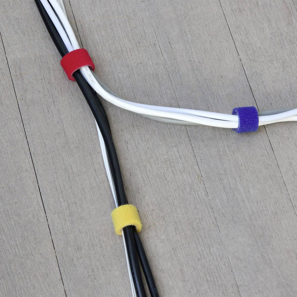 Kilka kabli jest związanych czerwonymi, żółtymi i niebieskimi opaskami rzepowymi na drewnianej podłodze.