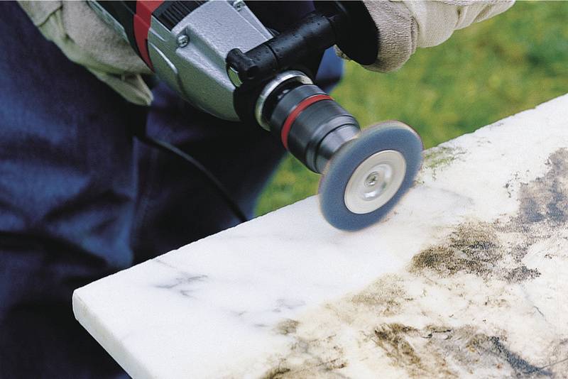 Osoba poleruje krawędź płyty marmurowej elektryczną szlifierką, aby wykończyć powierzchnię.