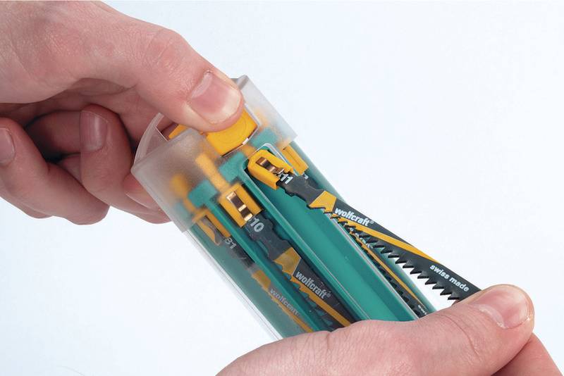 Dwie ręce trzymają cylindryczny pojemnik z różnymi piłami. Jedna ręka obraca nakrętkę u góry pojemnika.