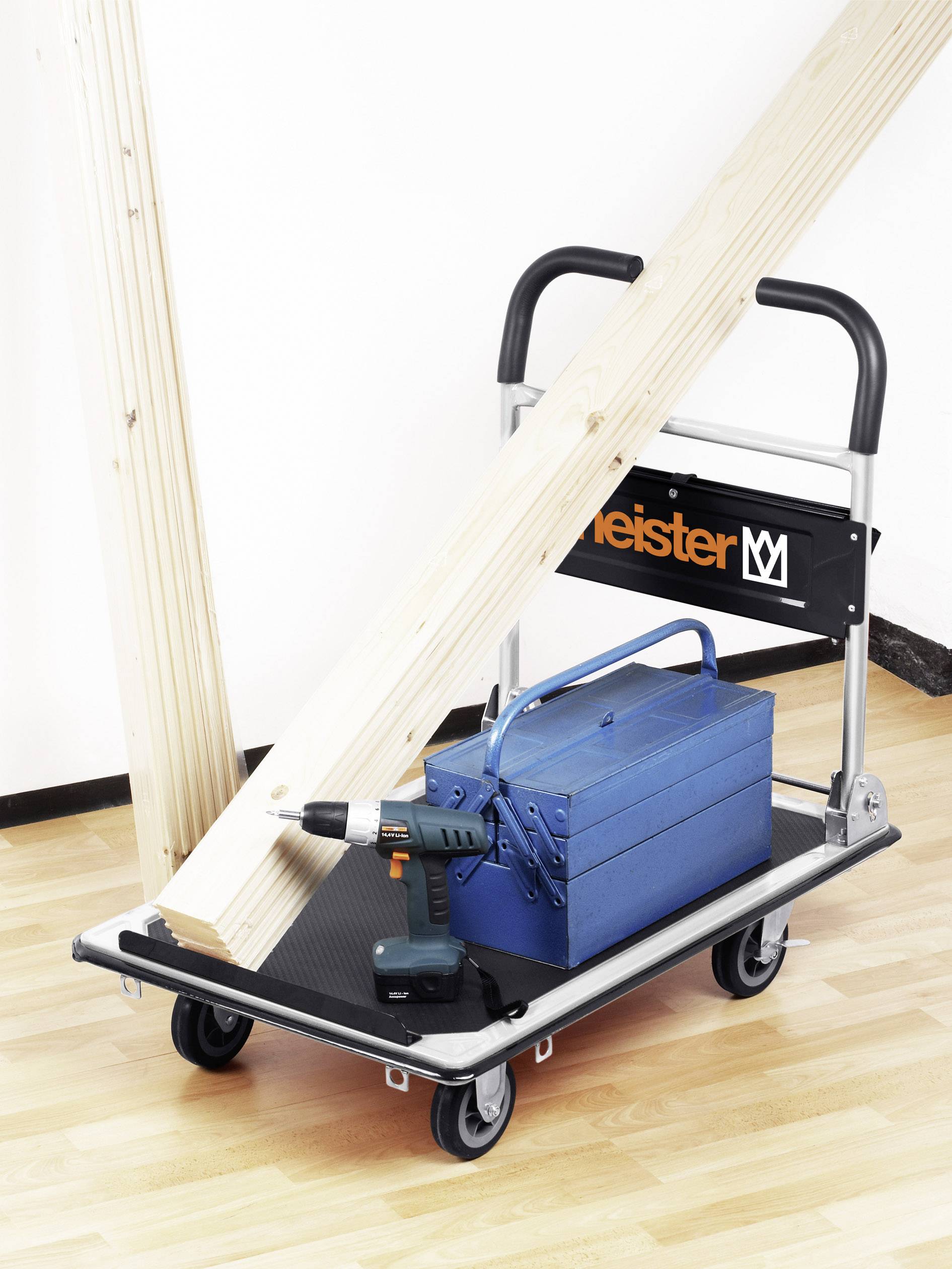 Wózek transportowy z drewnianymi belkami, niebieską skrzynką narzędziową i akumulatorowym wkrętarką na podłodze parkietowej.