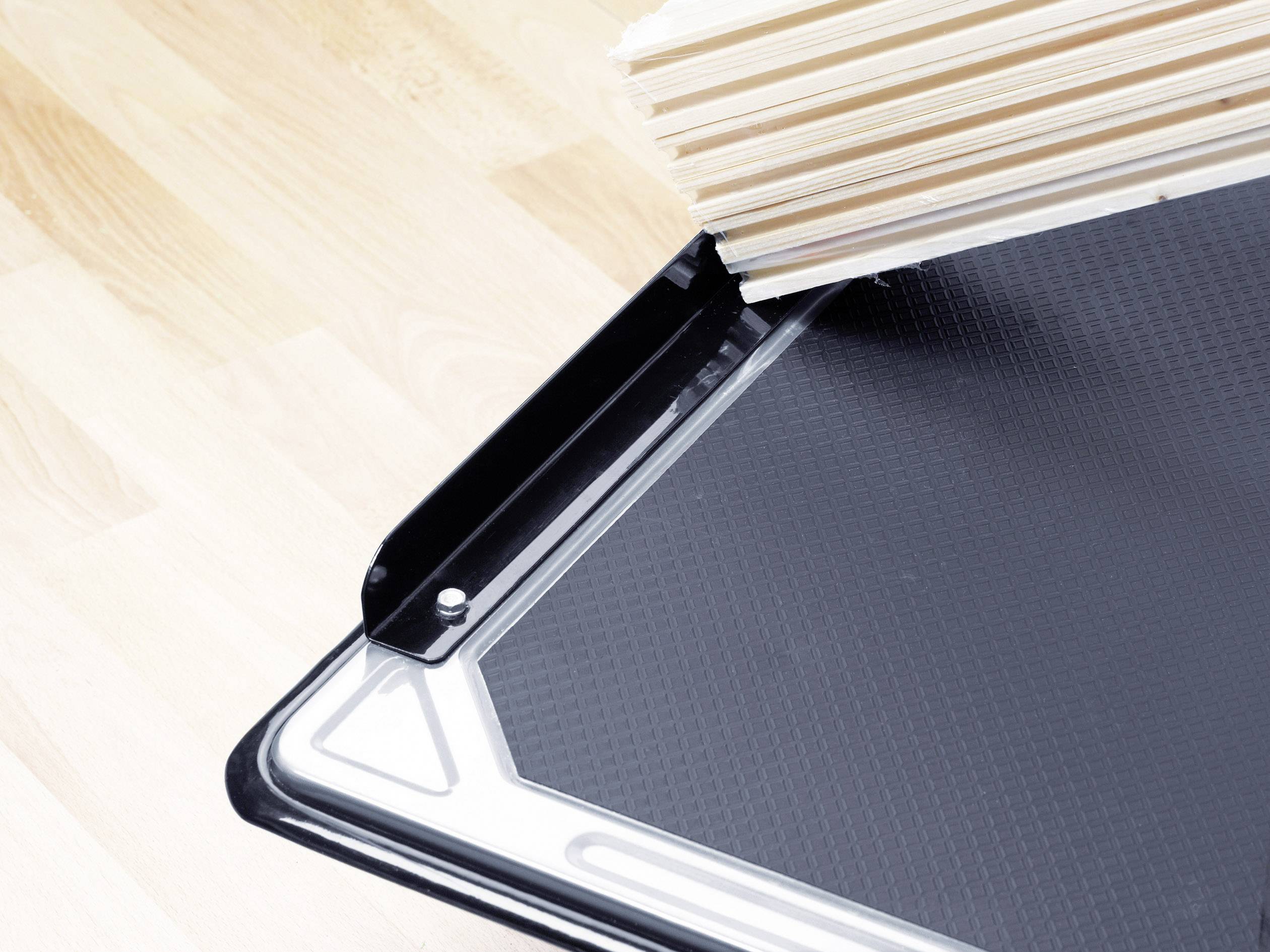 Czarna taca z podwyższoną krawędzią przytrzymuje kilka drewnianych listew na jasnej drewnianej powierzchni.