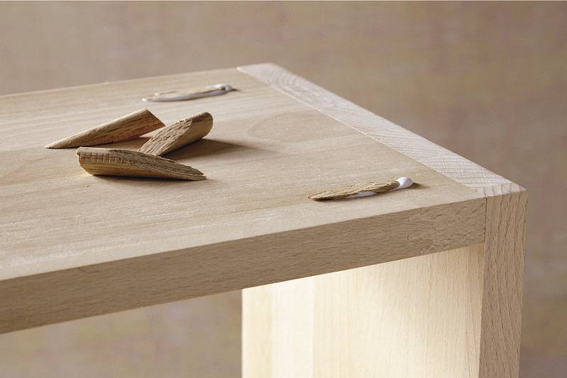 Drewniany stół z odłamanymi fragmentami drewna i widocznymi śladami kleju na krawędzi, wskazującymi na uszkodzoną lub niedokończoną naprawę.