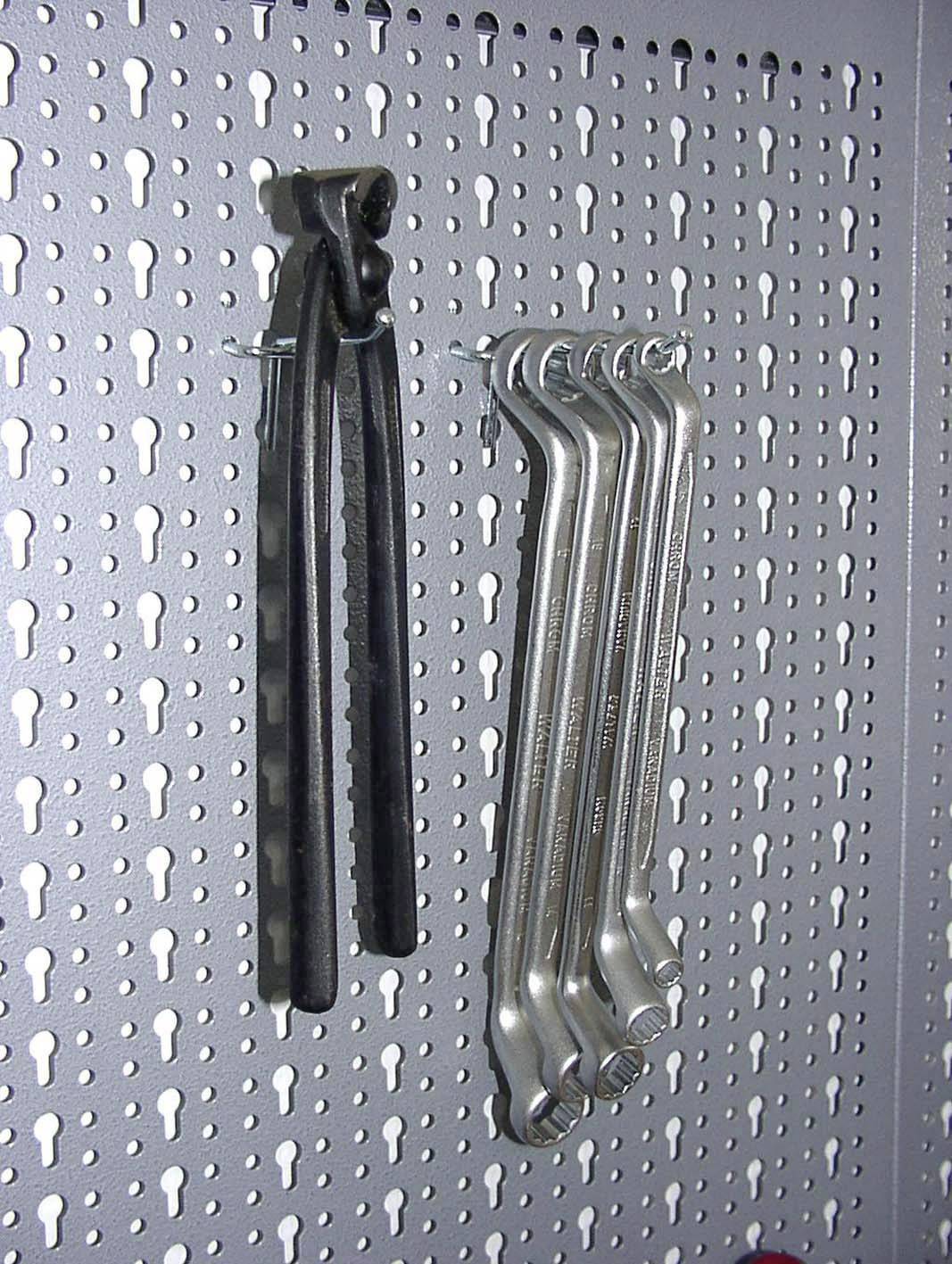 Dwa komplety kluczy nastawnych wiszą w uporządkowany sposób na metalowej tablicy perforowanej w warsztacie.