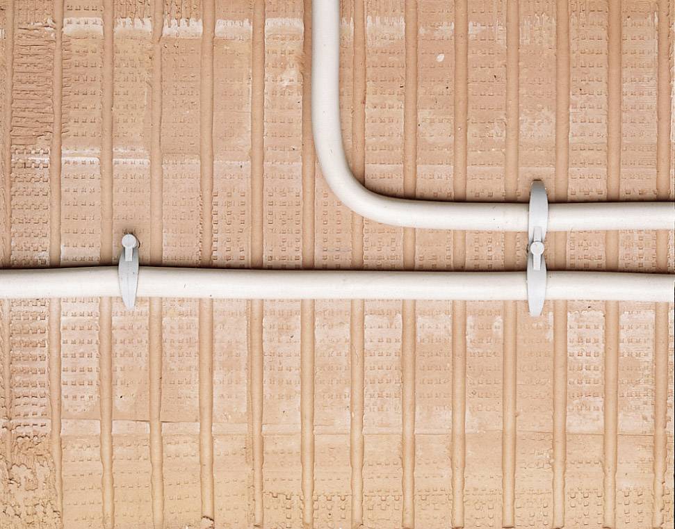 Dwa białe rury biegną równolegle wzdłuż strukturalnej czerwonej ściany z cegły i są zamocowane metalowymi uchwytami.