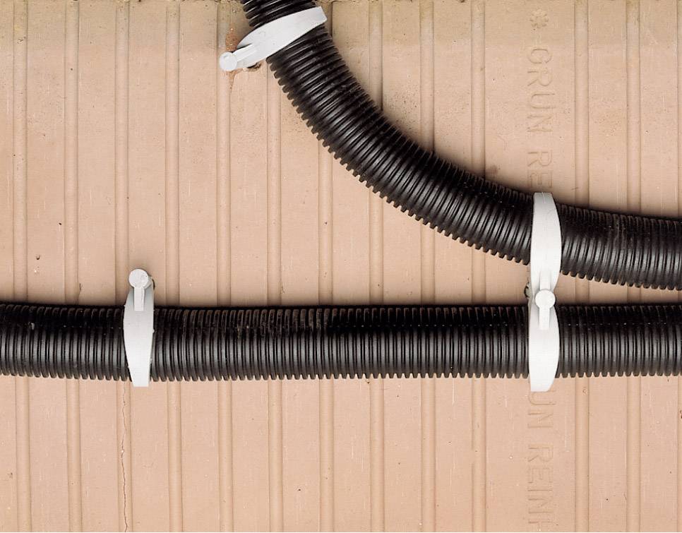 Dwa czarne, elastyczne przewody kablowe są przymocowane białymi opaskami kablowymi do falistej, pomarańczowej ściany.