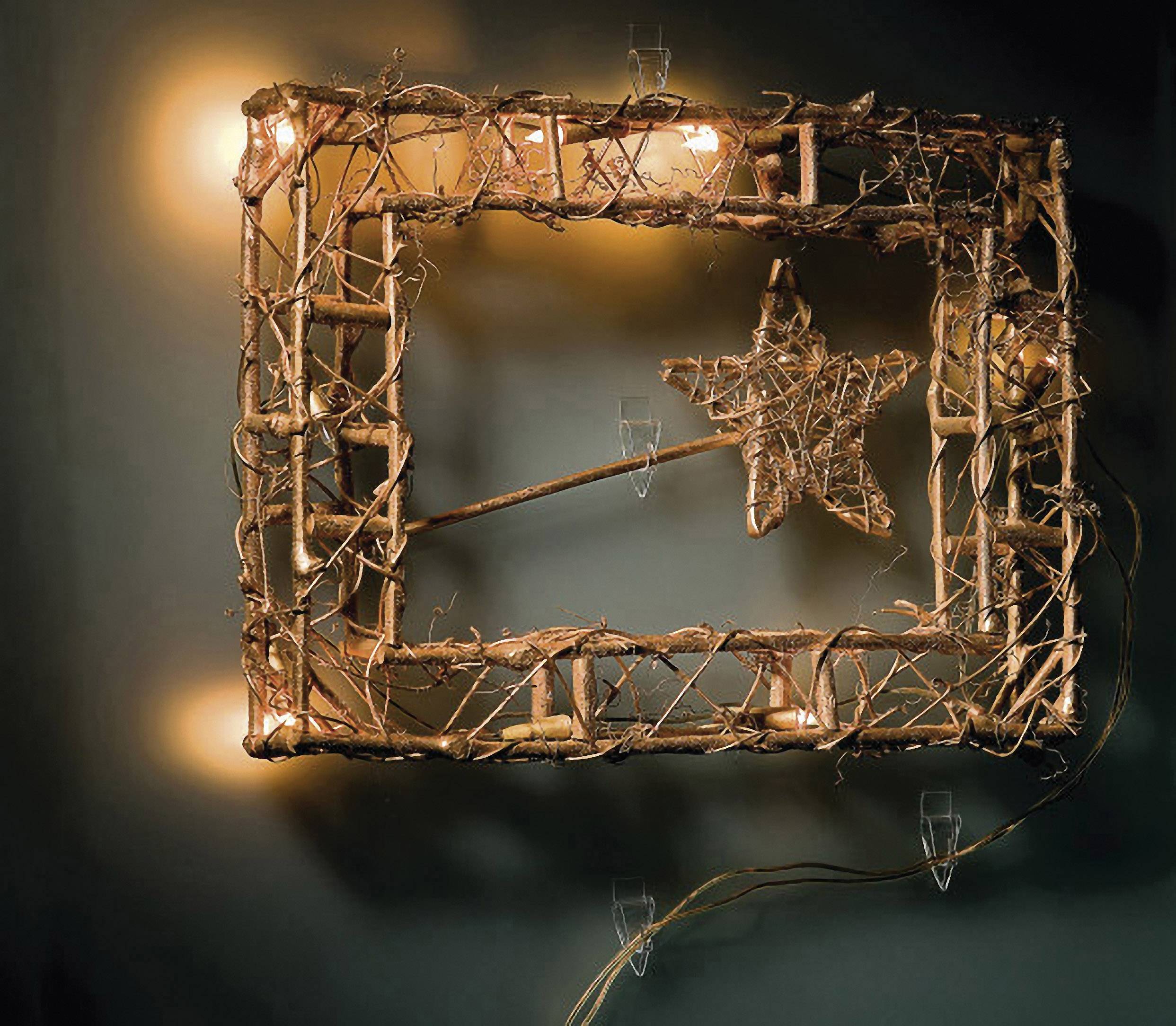 Prostokątna, świecąca drewniana rama z gwiazdą utworzoną z gałęzi pośrodku, zawieszona na ciemnej ścianie.