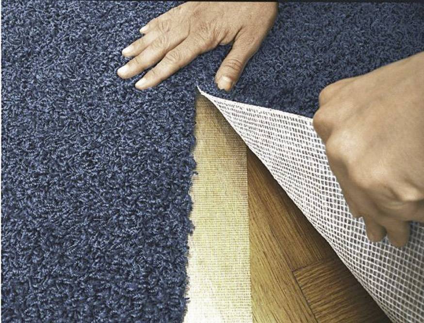 Osoba kładzie niebieski dywan na drewnianej podłodze, wygładzając krawędzie i starannie go rozwijając.