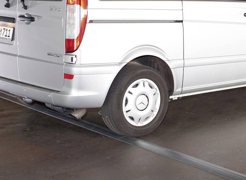 Srebrny dostawczak z logo Mercedes stoi zaparkowany, a jedno z jego kół przejeżdża przez metalowy próg na podłożu.