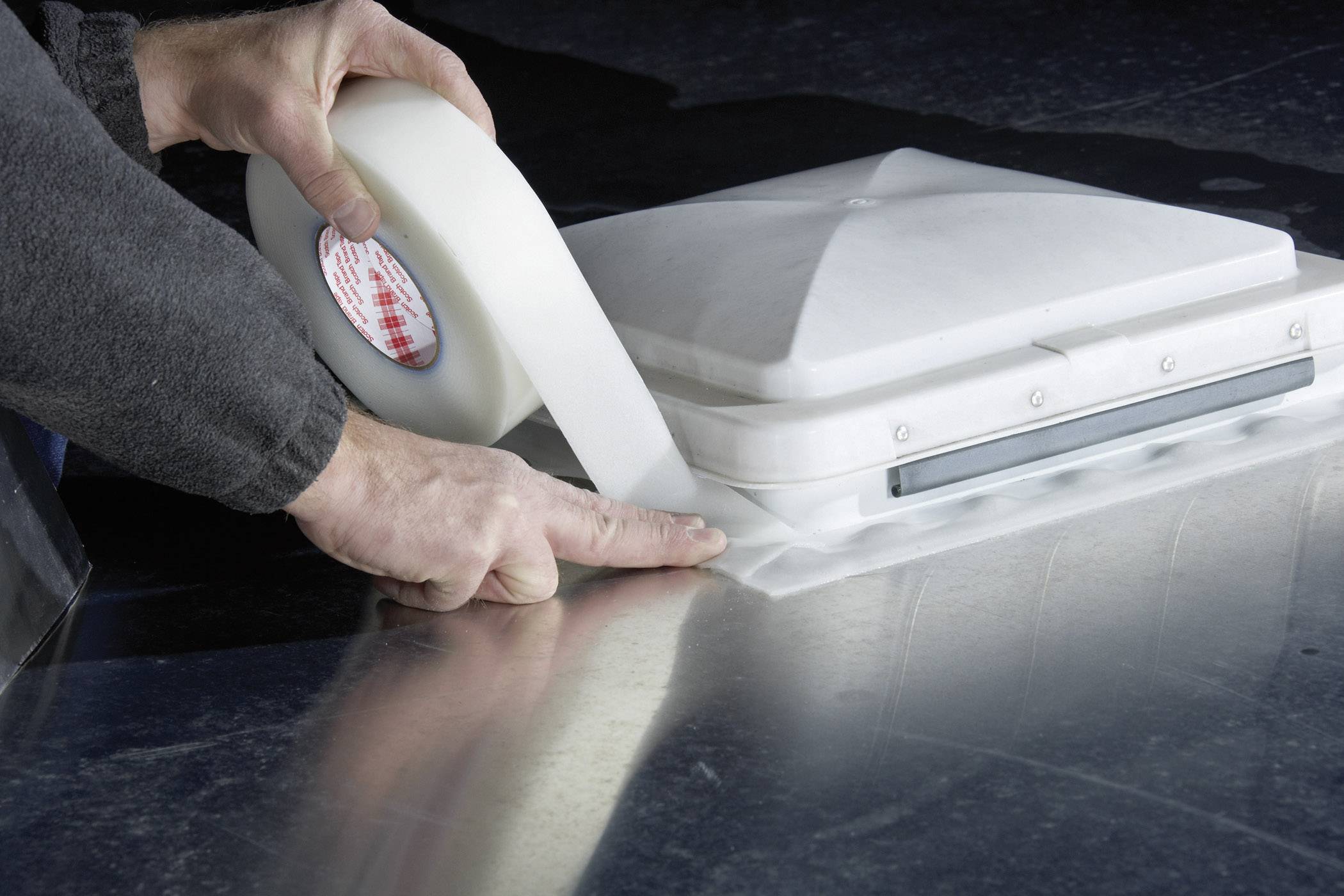 Ręce osoby naklejają białą taśmę uszczelniającą na srebrną powierzchnię metalową, aby zamocować białą osłonę z tworzywa sztucznego.