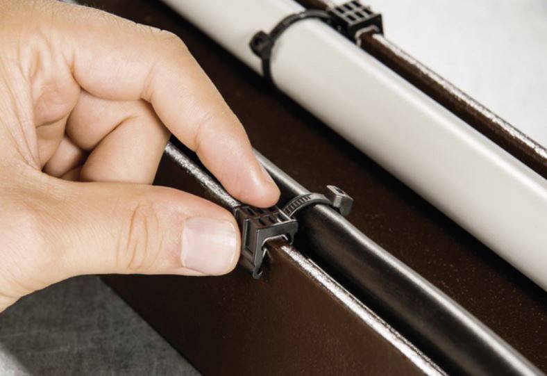 Ręka mocująca kabelkę na czarnym kablu w kanale kablowym. Obok znajduje się kolejny biały kabel.