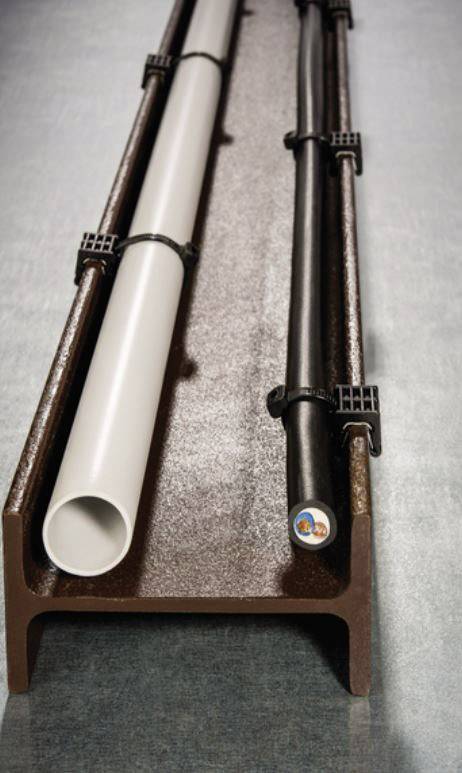 Metalowy kanał zawiera dwie równolegle prowadzone rury, jedną białą i jedną czarną, które są przymocowane zaciskami.