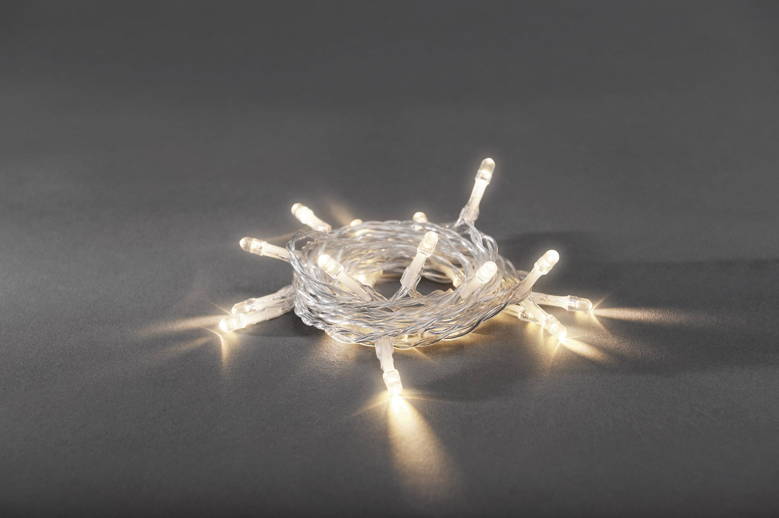 Łańcuch świetlny z białych lamp LED jest zwinięty na szarym tle i emituje ciepłe światło.