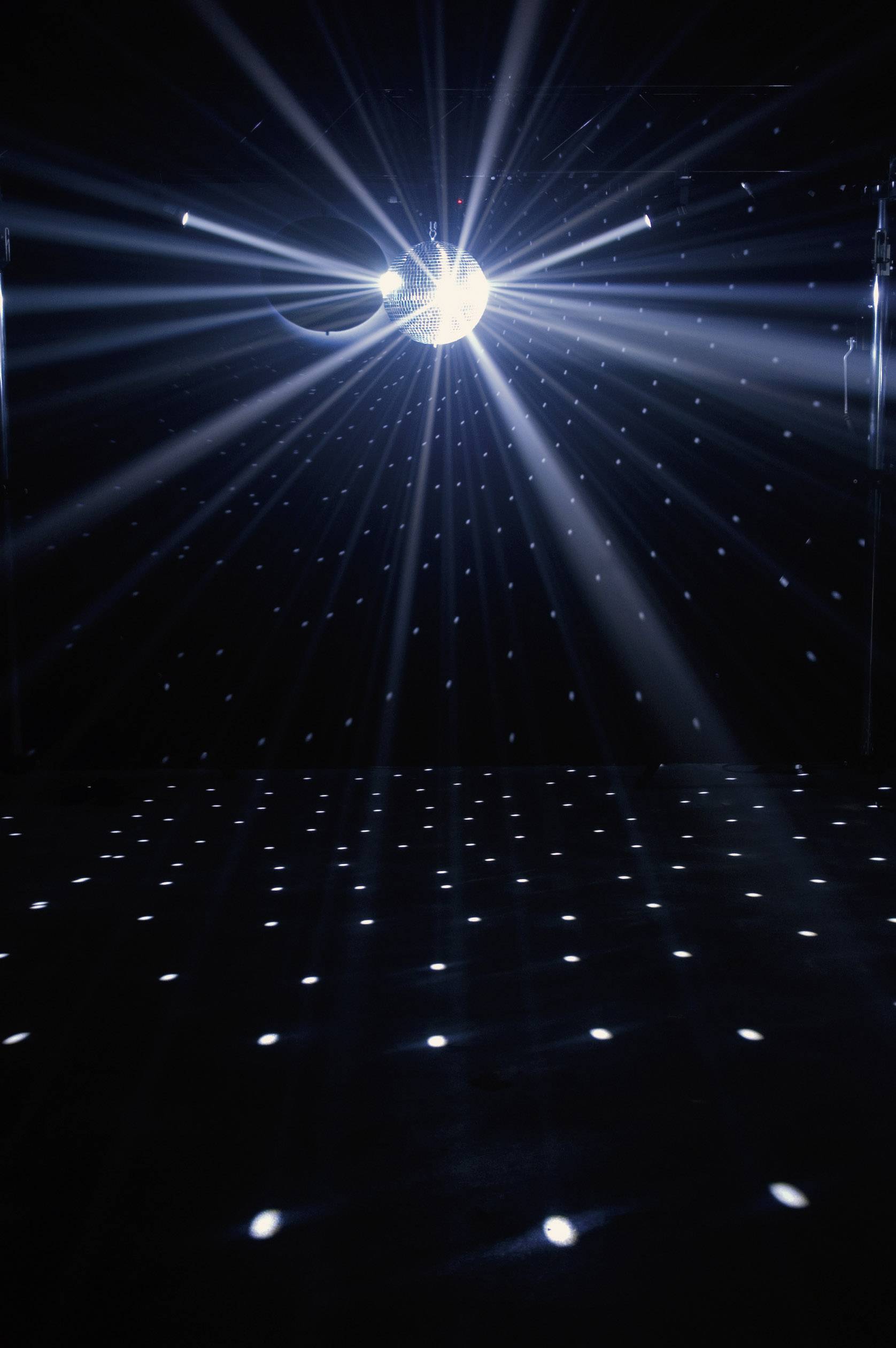 Kula dyskotekowa rzuca wiązki światła w ciemnym pomieszczeniu, tworząc błyszczący efekt na podłodze.