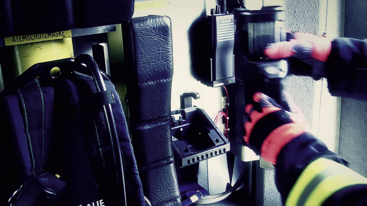 Strażak w odzieży ochronnej reguluje sprzęt w pojeździe interwencyjnym. Widoczne są rękawice ochronne i wyposażenie.