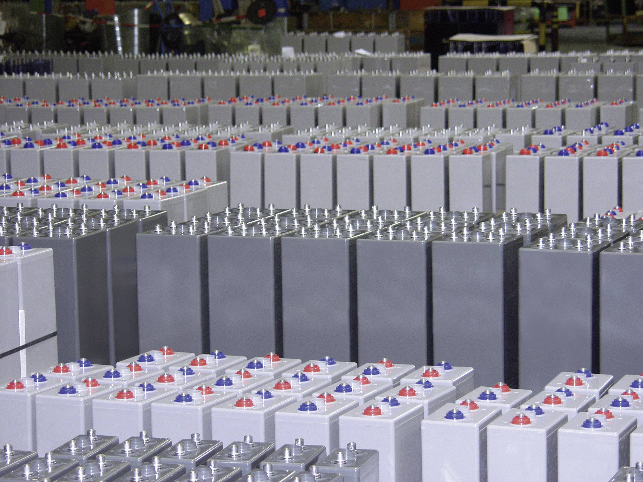 Rzędy szarych baterii przemysłowych w środowisku fabrycznym, ułożone w stosy i gotowe do wysyłki.