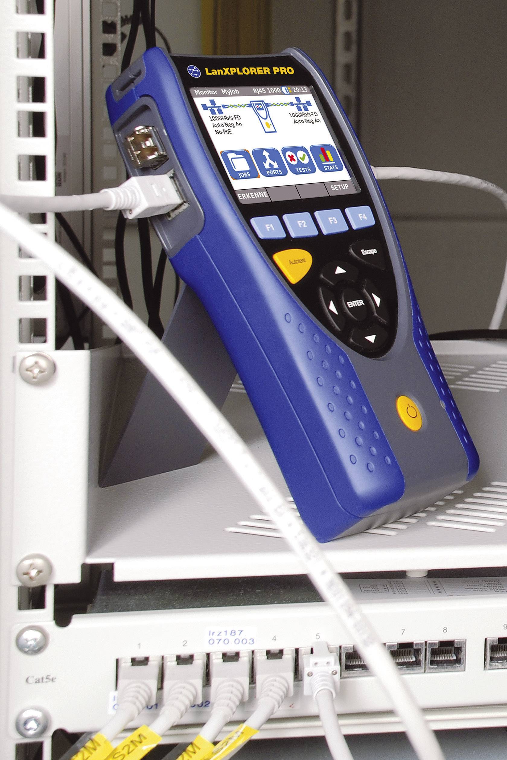 Tester sieci z podłączonym kablem wyświetla różne analizy sieciowe na ekranie. W tle widoczne są urządzenia serwerowe.