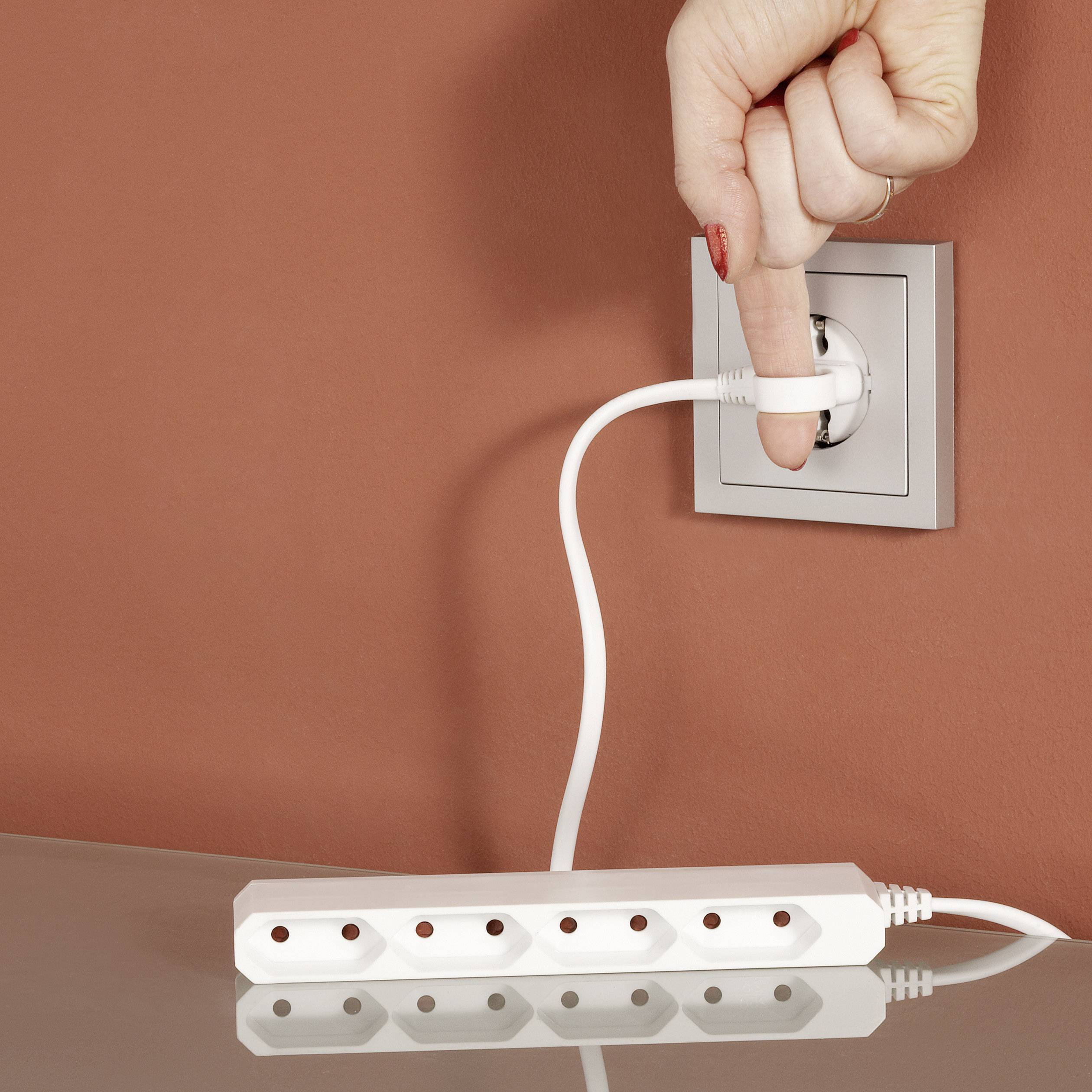 Dłoń wyciąga wtyczkę sieciową z gniazdka elektrycznego, podczas gdy przewód przedłużający spoczywa na stole.
