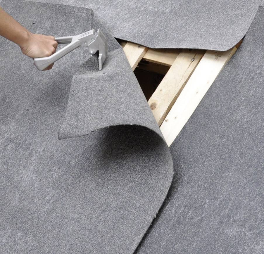 Ktoś przybija szary dywan do drewnianej deski.