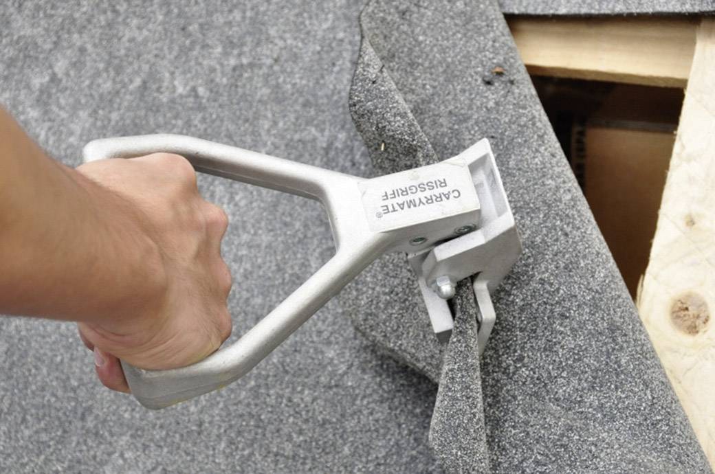 Jedna ręka używa narzędzia do zdejmowania klamerek, podnosząc dywan, pod którym widoczna jest drewniana podłoga.