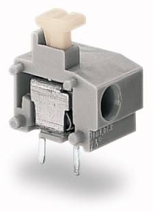 Szary elektroniczny przełącznik z dwoma metalowymi pinami u dołu oraz jaśniejszym przyciskiem aktywacyjnym na górze, na białym tle.