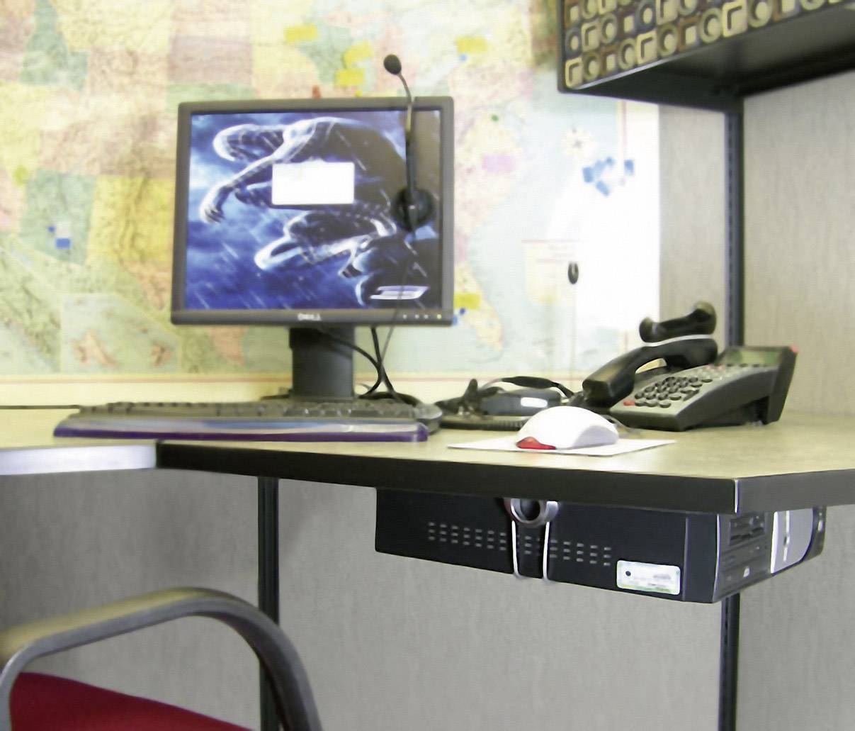 Biurko z ekranem komputera, klawiaturą, myszą, telefonem i zestawem słuchawkowym. W tle mapa świata.