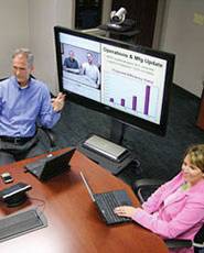 Spotkanie dwóch osób przy stole. Na ekranie wyświetlana jest prezentacja z diagramem "Aktualizacja operacji i produkcji".