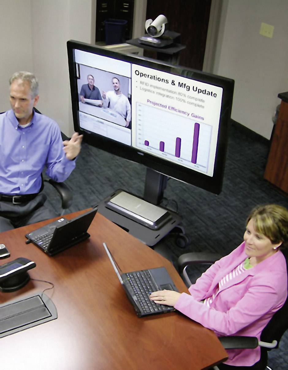 Trzech osób siedzi w sali konferencyjnej, patrząc na ekran z prezentacją. Slajd przedstawia dwóch mężczyzn i diagram.