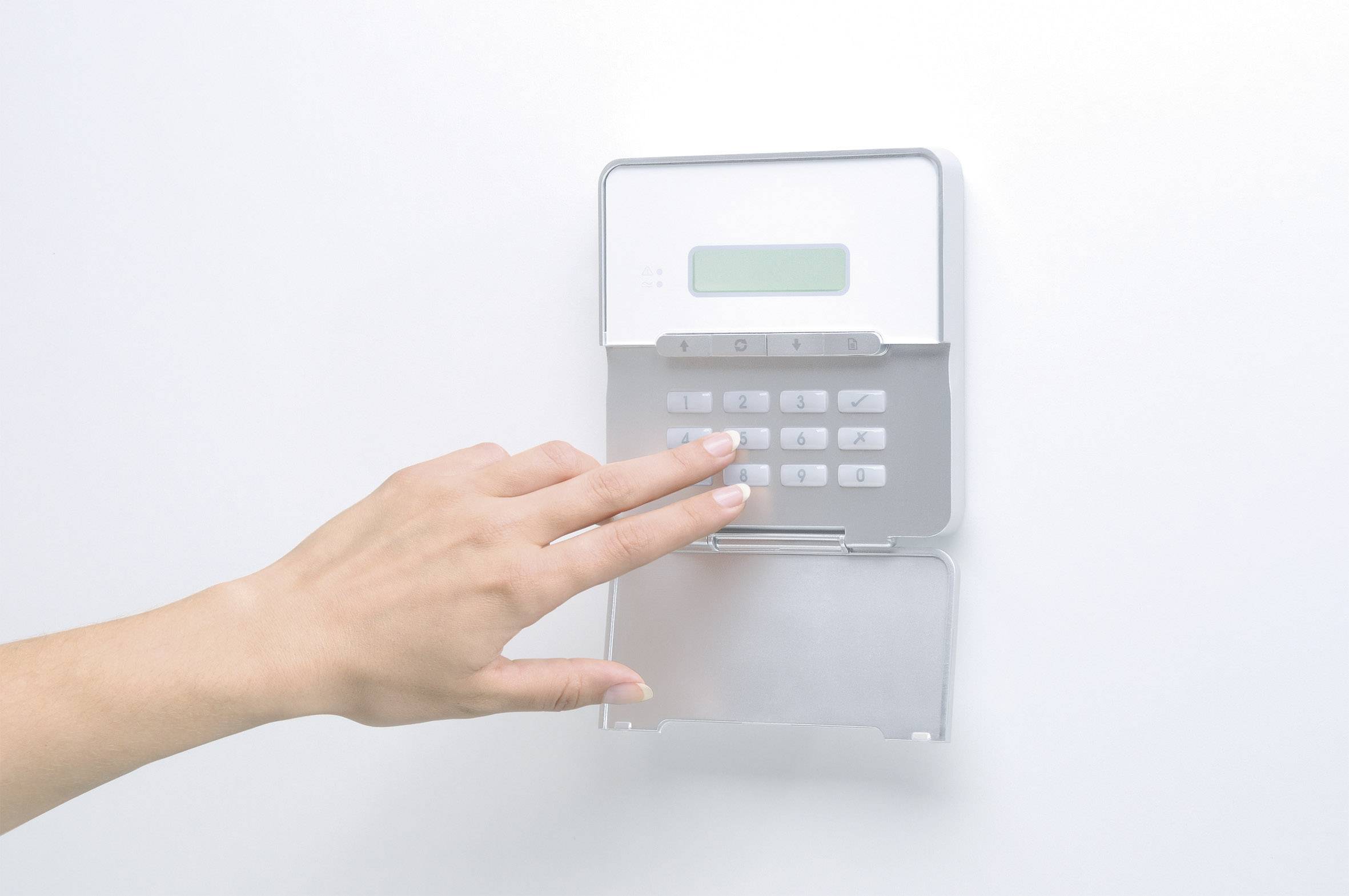 Dłoń naciska pole wprowadzania kodu bezpieczeństwa w systemie alarmowym lub zabezpieczającym zamontowanym na ścianie.