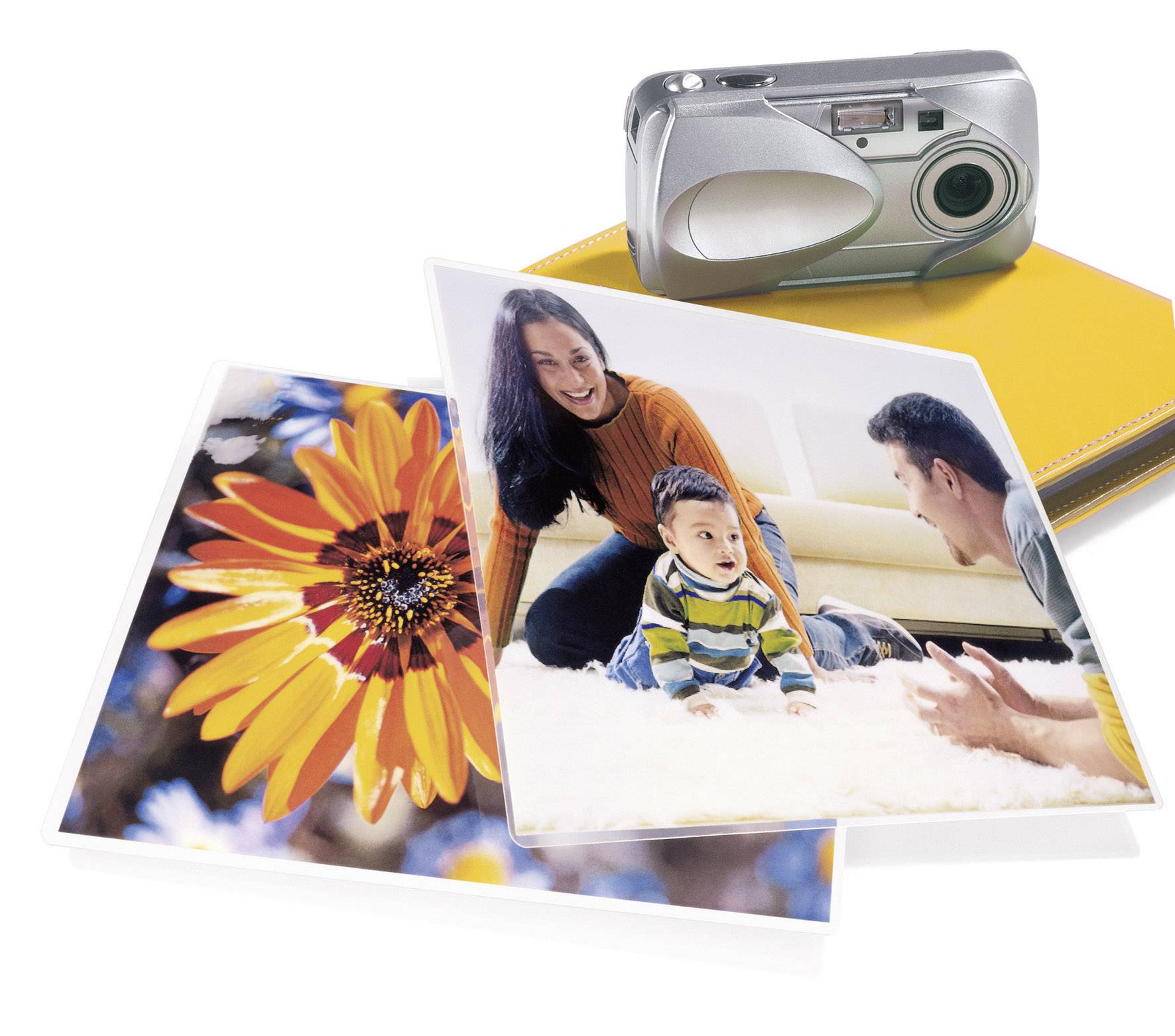 Srebrny aparat fotograficzny obok żółtego albumu. Dwa zdjęcia: jedno przedstawia świecący pomarańczowy kwiat, drugie rodzinę z niemowlęciem bawiącą się na dywanie.