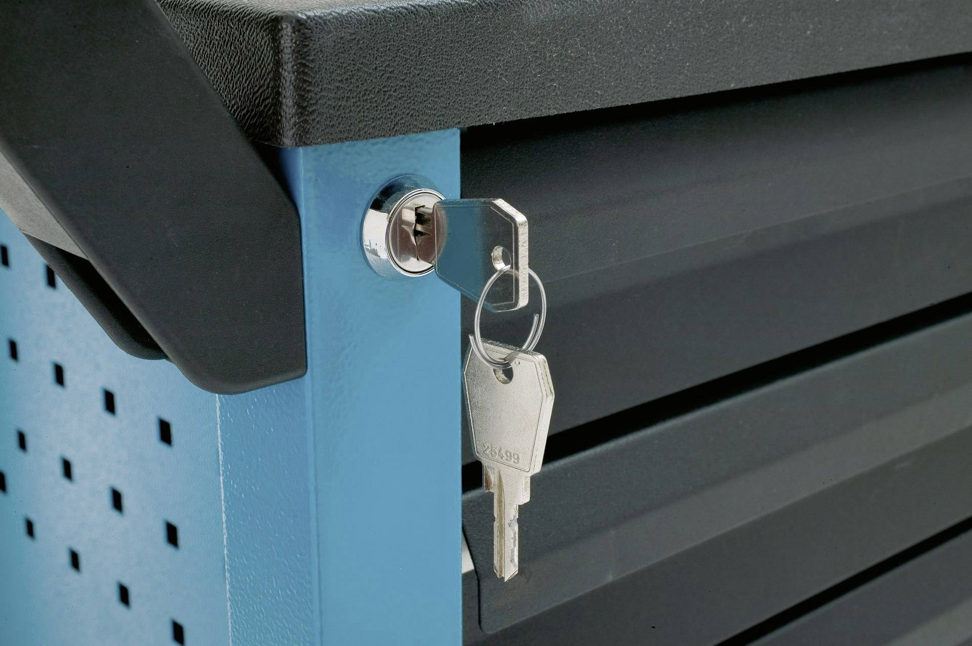Klucz tkwi w zamku niebieskiego wózka narzędziowego. Wózek posiada kilka szuflad i czarny uchwyt.
