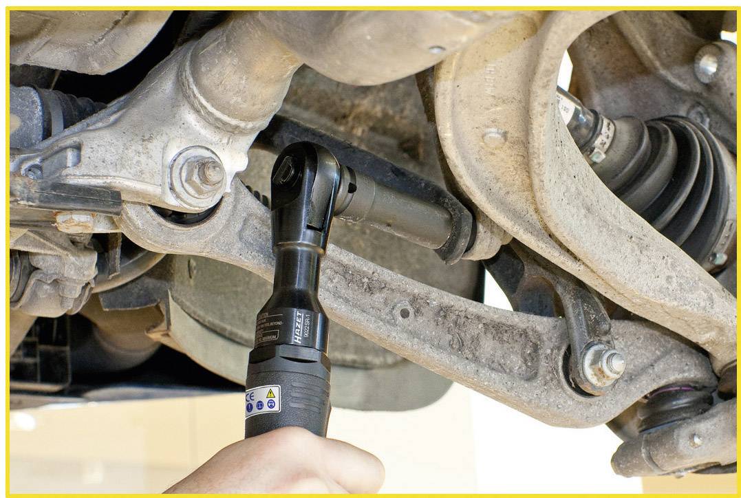 Jedna ręka trzyma elektryczny klucz dynamometryczny, który pracuje przy elemencie zawieszenia pojazdu.