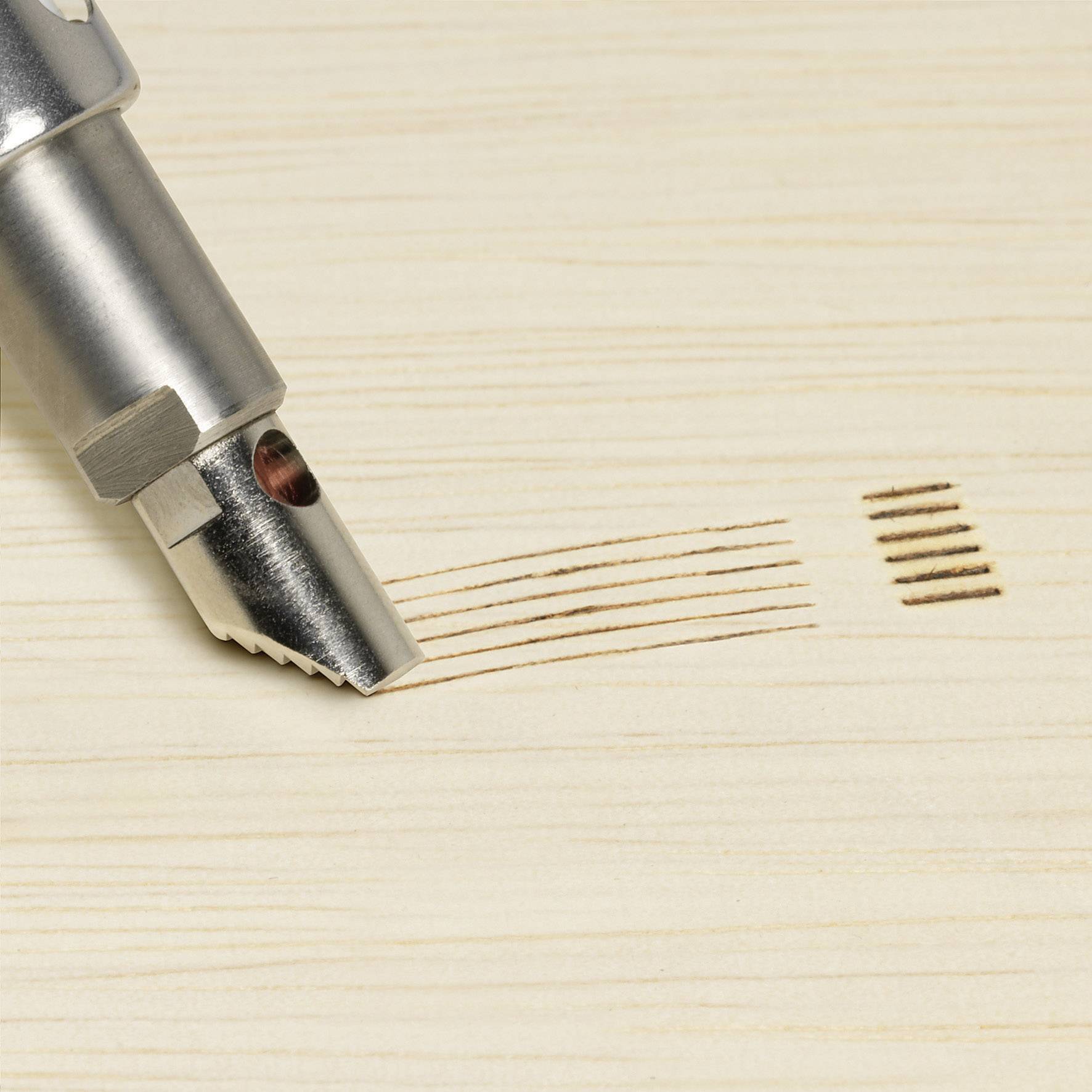 Zbliżenie frezu, który precyzyjnie wycina linie i rowki na jasnym drewnie. Na czubku wiertła widoczne są drobne wióry.