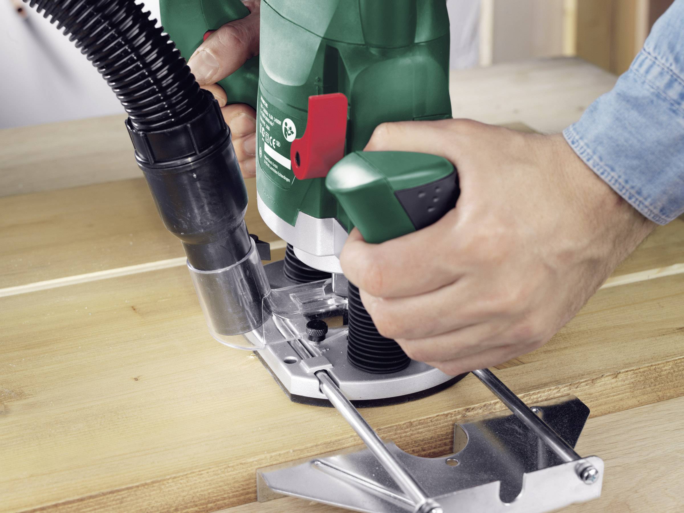 Zbliżenie osoby używającej zielonej frezarki górnowrzecionowej do obróbki powierzchni drewnianych. Narzędzie leży na drewnianej desce.