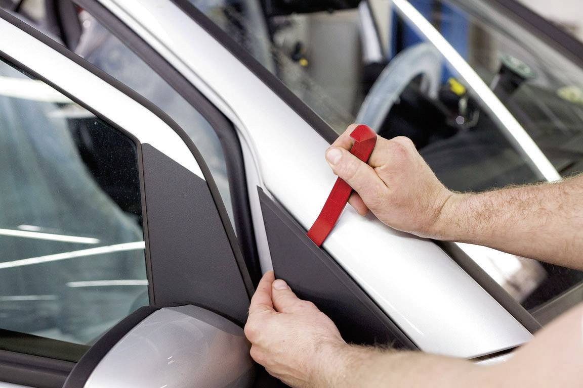 Osoba usuwa tapicerkę drzwi srebrnego samochodu za pomocą czerwonego plastikowego narzędzia.