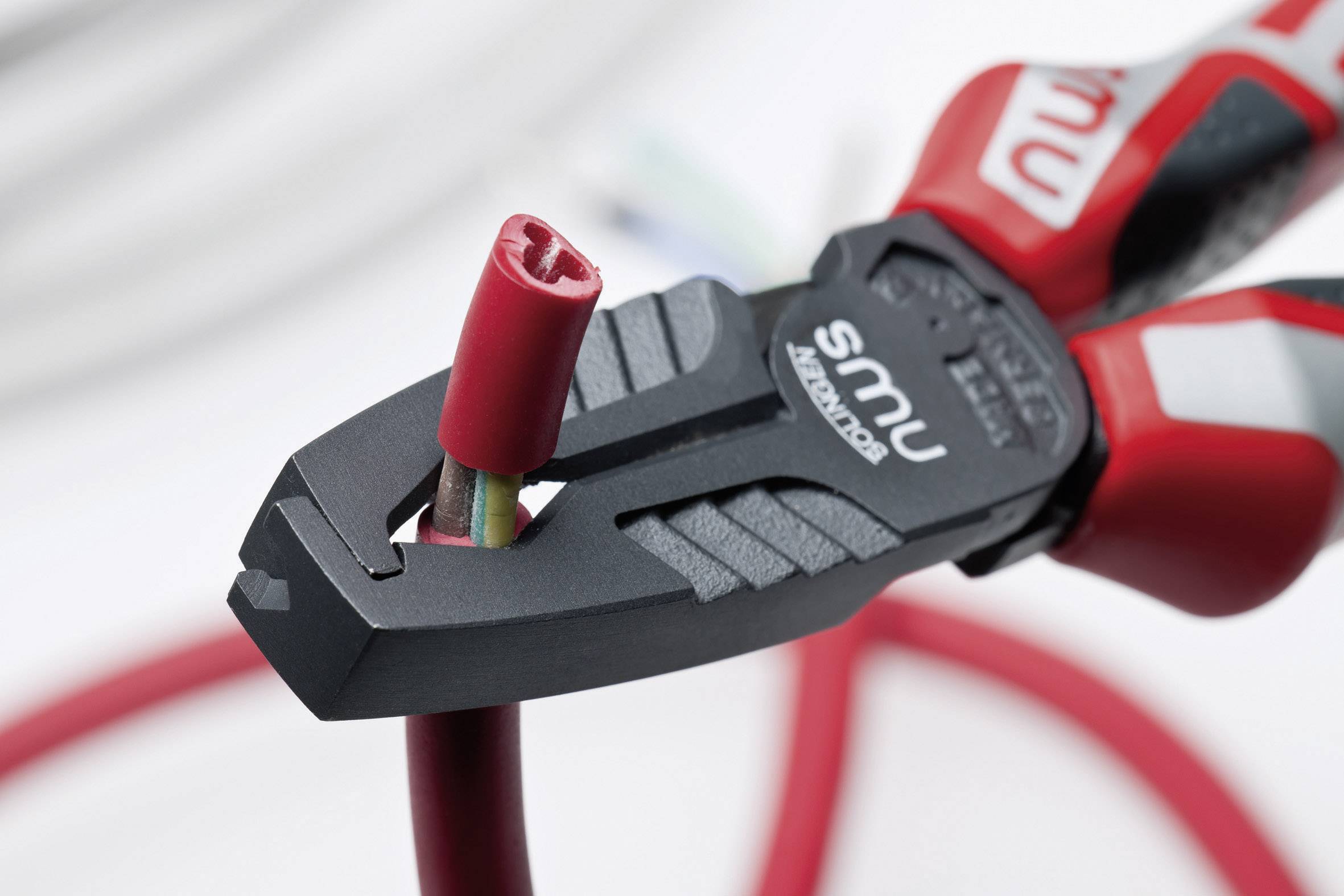 Szczypce przecinające czerwony kabel z podłączoną osłoną. Szczypce są czarno-czerwone i leżą na jasnym tle.