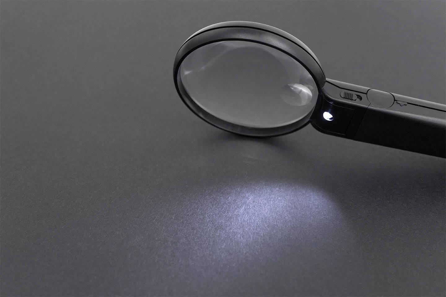 Lupa z wbudowaną lampką LED rzuca światło na szarą powierzchnię.