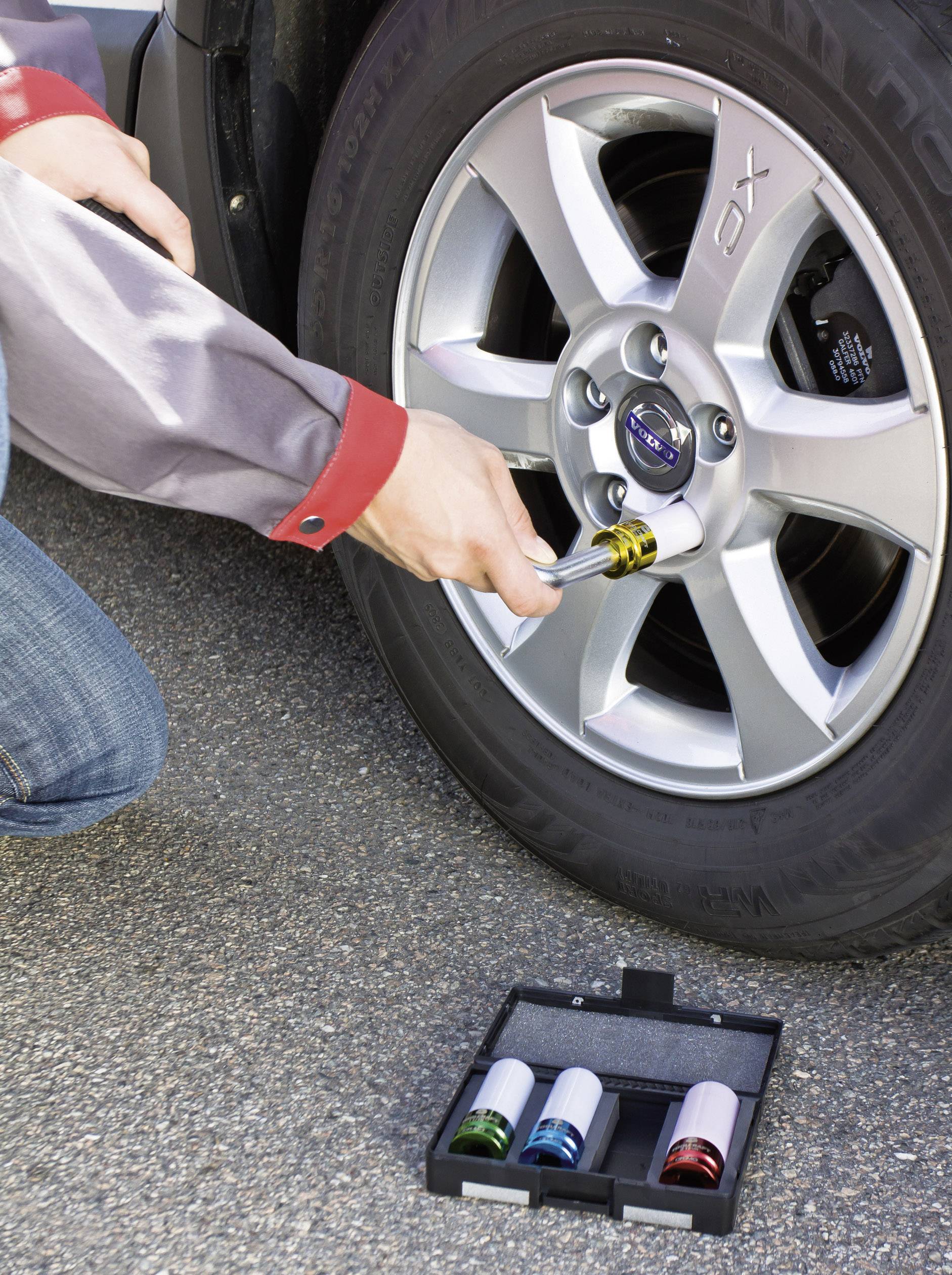 Mężczyzna dokręca nakrętki kół samochodu kluczem dynamometrycznym. Przed nim leży zestaw kolorowych nasadek.