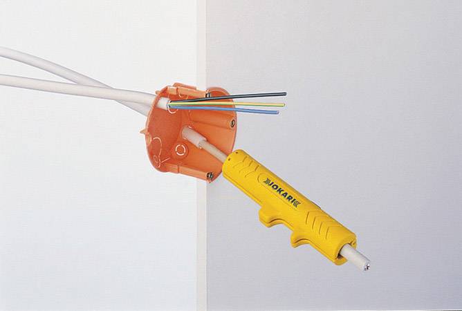 'Narzędzie tnie kabel' do puszki elektrycznej. Żółte narzędzie trzyma kilka kabli wystających z pomarańczowej puszki.