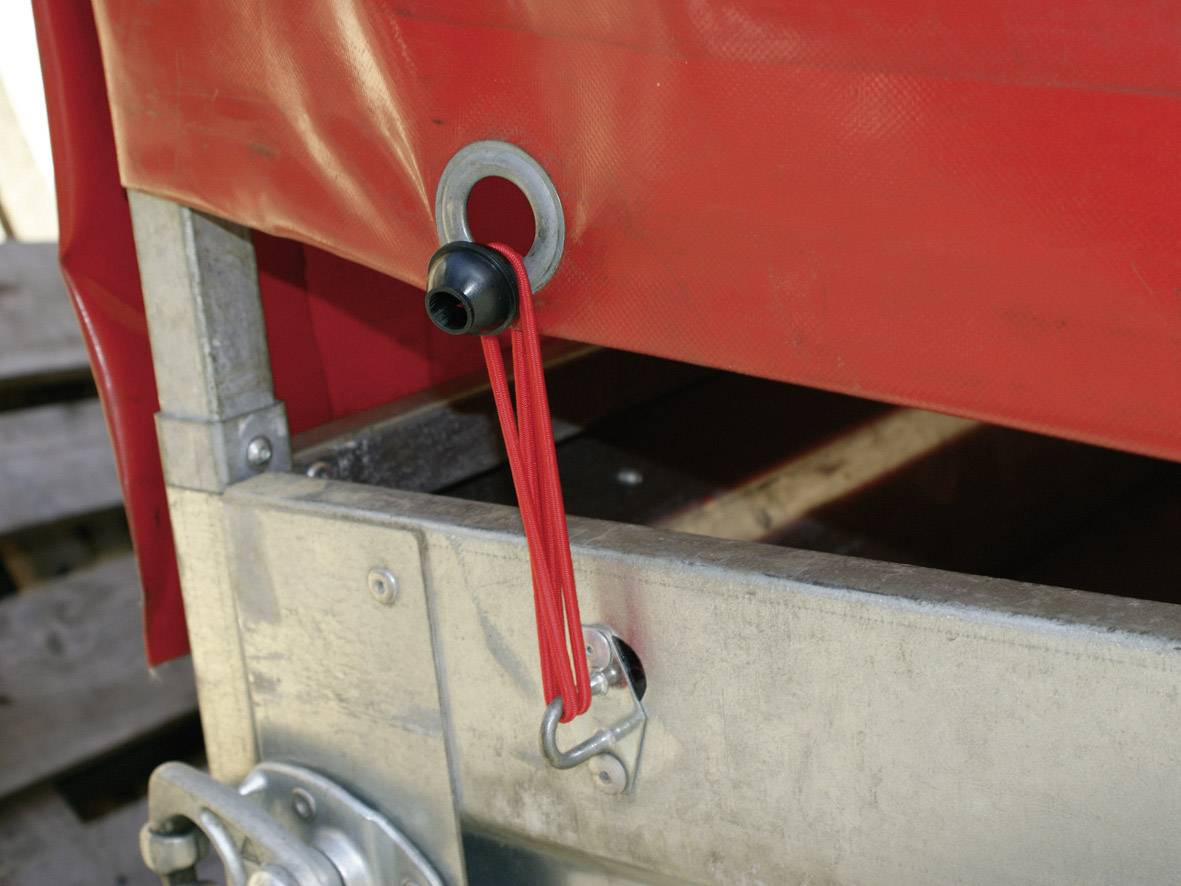 Czerwona elastyczna gumka jest zamocowana do metalowej pętli i rozciągnięta na haku przy krawędzi metalowej powierzchni.