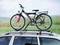 Rower na bagażniku dachowym samochodu, zaparkowany na polu z zieloną krajobrazem w tle.