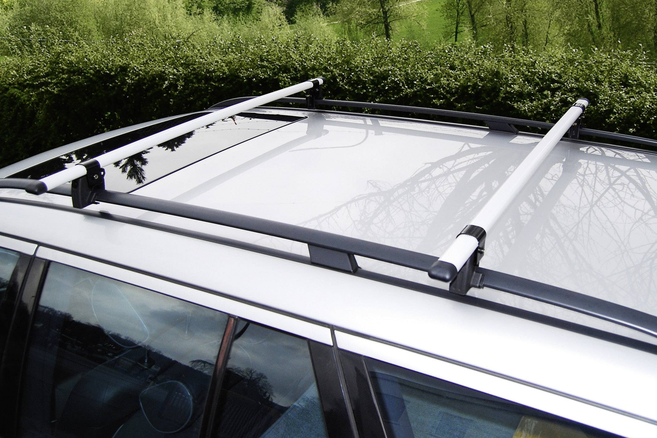 Samochód z bagażnikami dachowymi, odpowiedni do przewozu rowerów lub bagażu. W tle drzewa i krzewy.