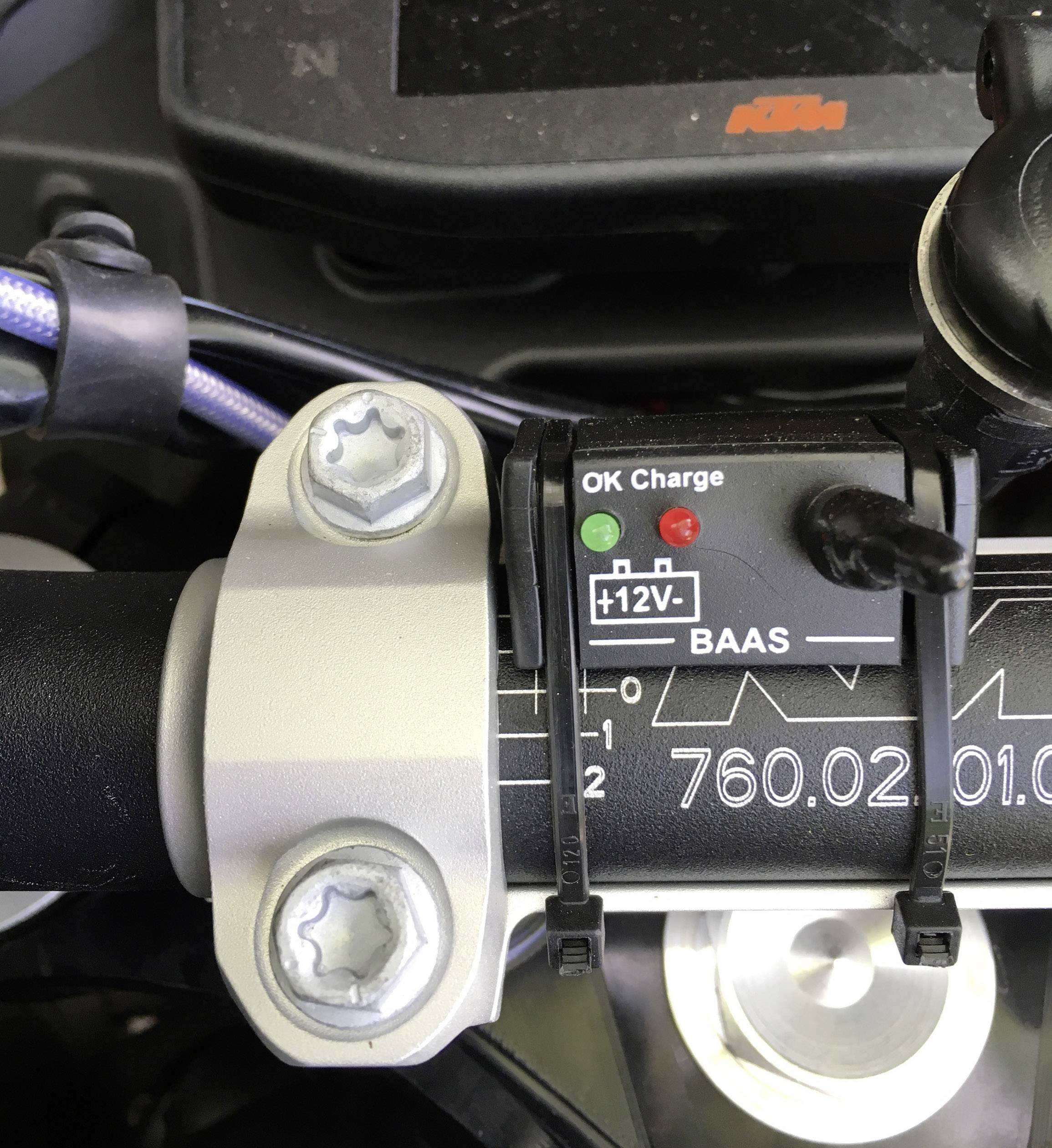 Motocyklowy kokpit z wyświetlaczem stanu naładowania baterii. Wskazuje, że ładowanie jest 'OK'. Widoczne są kabel i kierownica.