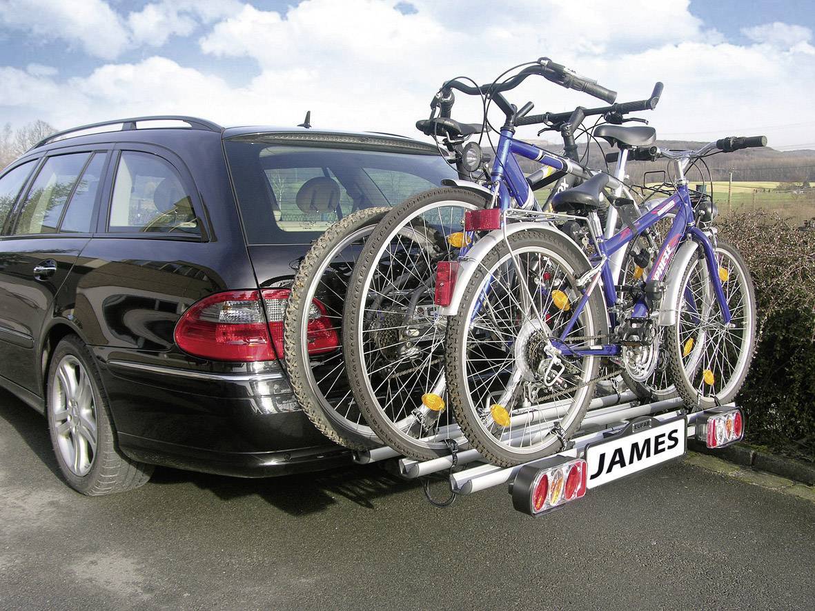 Czarny kombi z dwoma rowerami zamontowanymi na tylnym bagażniku, z tablicą rejestracyjną 'JAMES', zaparkowany przy krawędzi drogi.