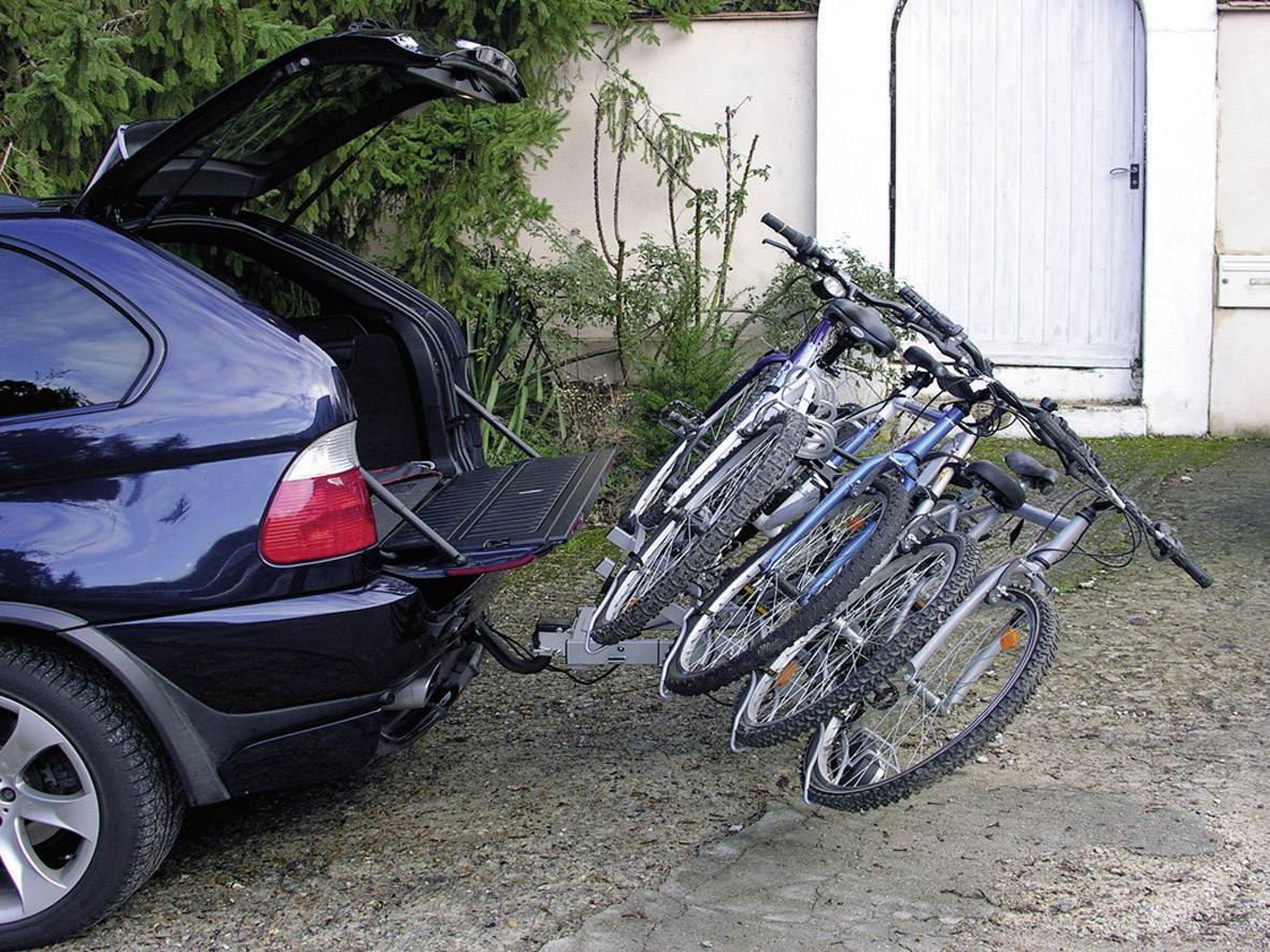 Samochód z otwartą bagażnikiem i czterema rowerami na tylnym bagażniku. Stoi na parkingu przed bramą.