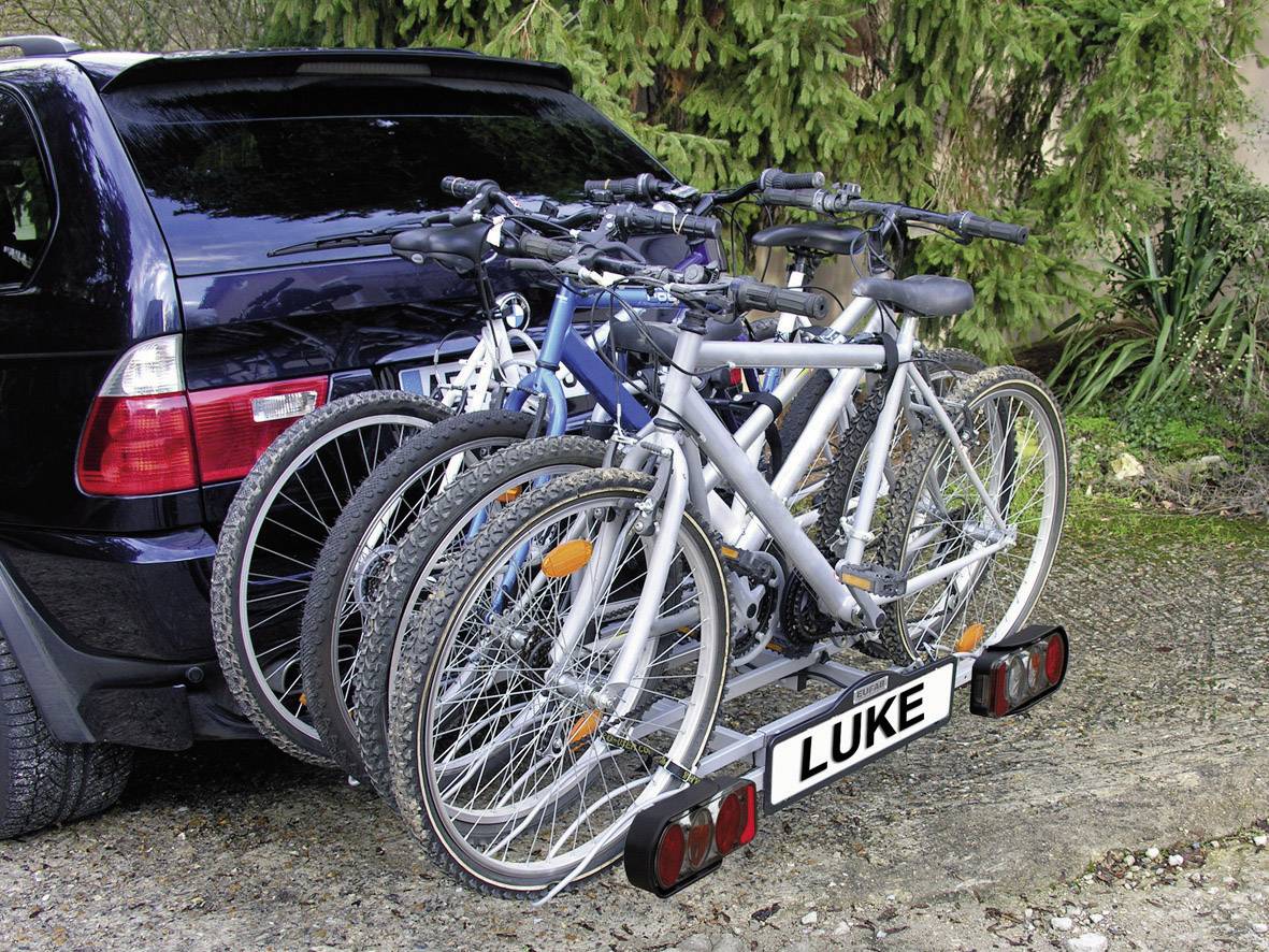 Samochód stoi na leśnej drodze. Z tyłu pojazdu zamontowane są cztery rowery na bagażniku rowerowym.