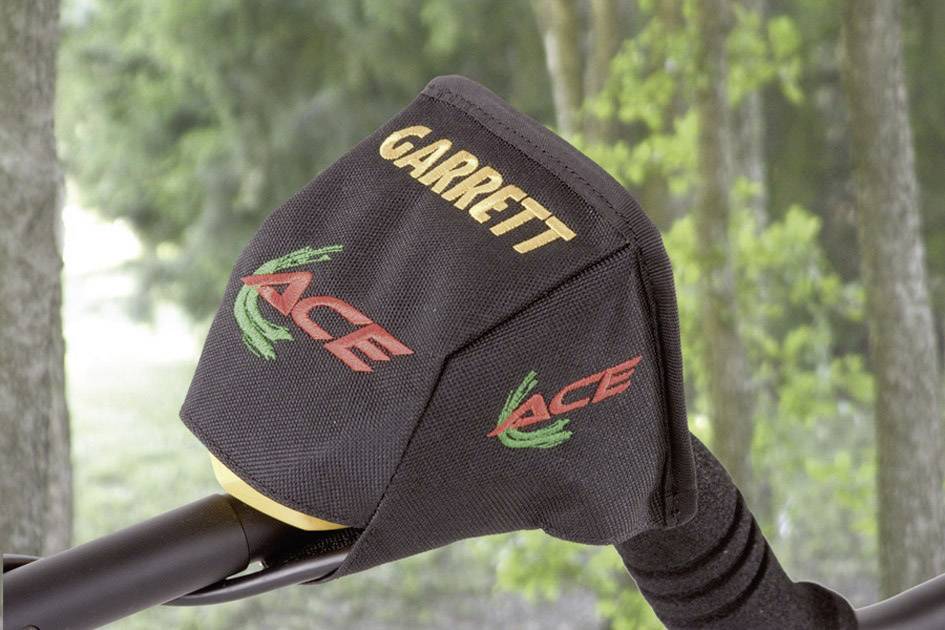 Sonda metalowa z logo 'GARRETT' i 'ACE' na tle bogatego w drzewa krajobrazu.