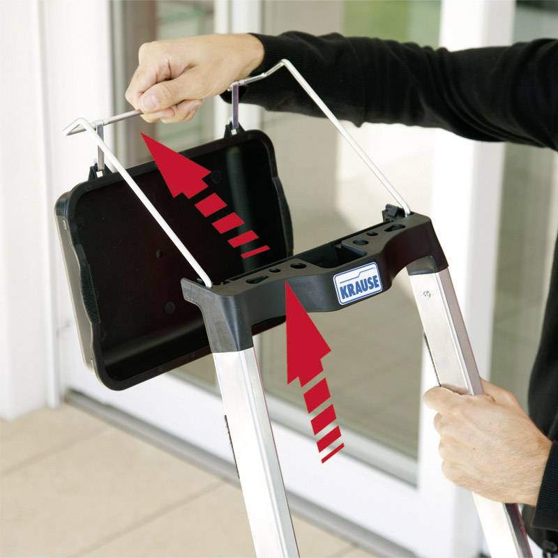 Mężczyzna mocuje półkę na składanej drabinie. Czerwone strzałki wskazują kierunek ruchu przy zakładaniu półki.