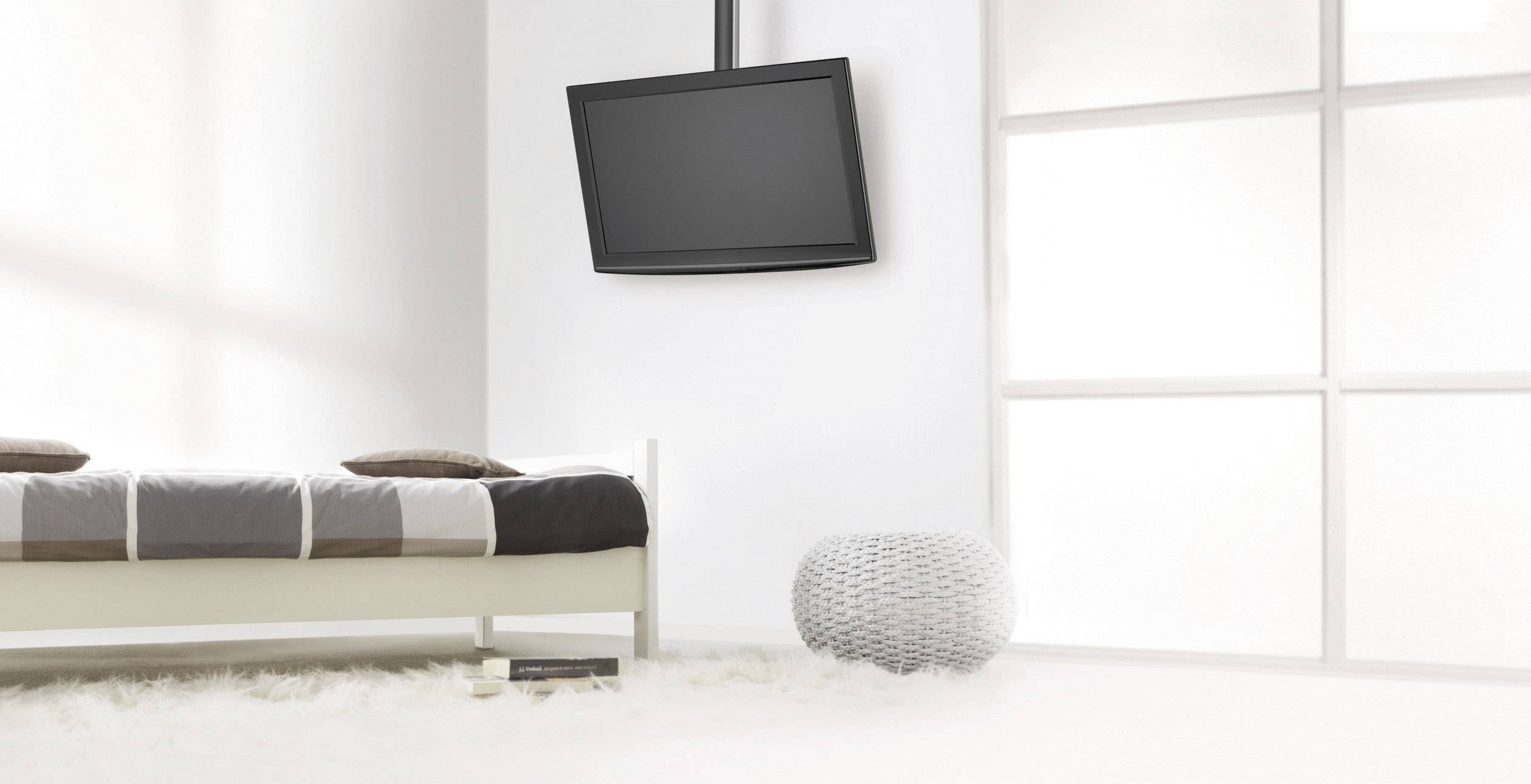 Minimalistyczna sypialnia z białym łóżkiem, telewizorem zamocowanym na ścianie i dużym oknem wpuszczającym dużo światła.